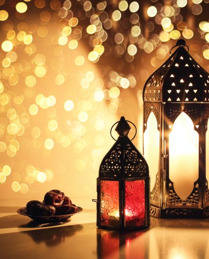 Ornamental Arabic lanterns with burning candles. Glittering golden bokeh lights. Plate with date fruit on the table. Greeting card for Muslim holiday Ramadan Kareem. Iftar dinner background. Ornamental Arabic lanterns with burning candles. Glittering golden bokeh lights. Plate with date fruit on the table. Greeting card for Muslim holiday Ramadan Kareem, iftar dinner background.