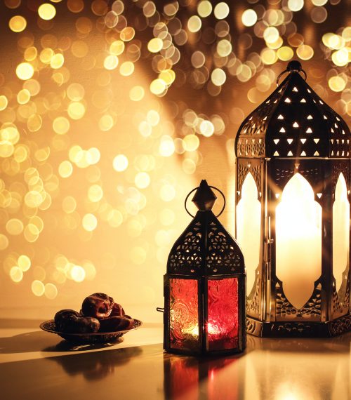 Ornamental Arabic lanterns with burning candles. Glittering golden bokeh lights. Plate with date fruit on the table. Greeting card for Muslim holiday Ramadan Kareem. Iftar dinner background. Ornamental Arabic lanterns with burning candles. Glittering golden bokeh lights. Plate with date fruit on the table. Greeting card for Muslim holiday Ramadan Kareem, iftar dinner background.